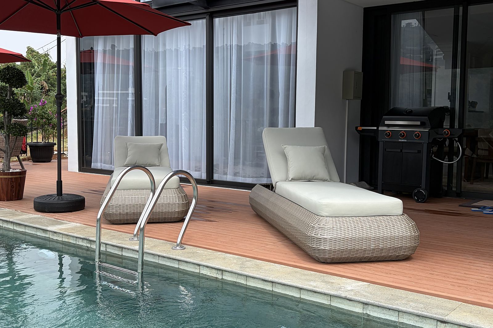 A daybed and a red parasol on the timber deck at the pool's edge